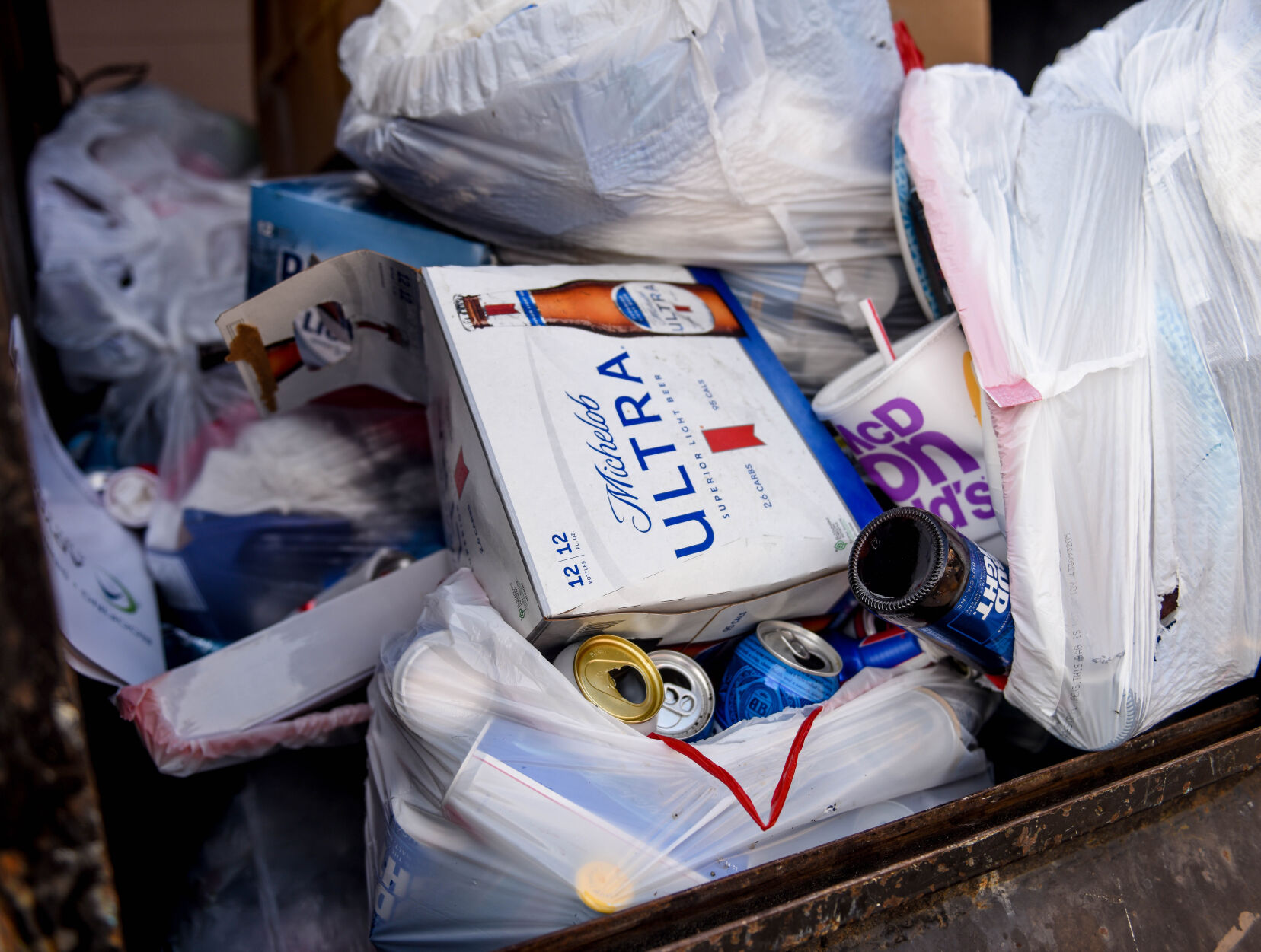 Several trash bags of beer bottles, empty cases of beer and trash lie in a residential dumpster